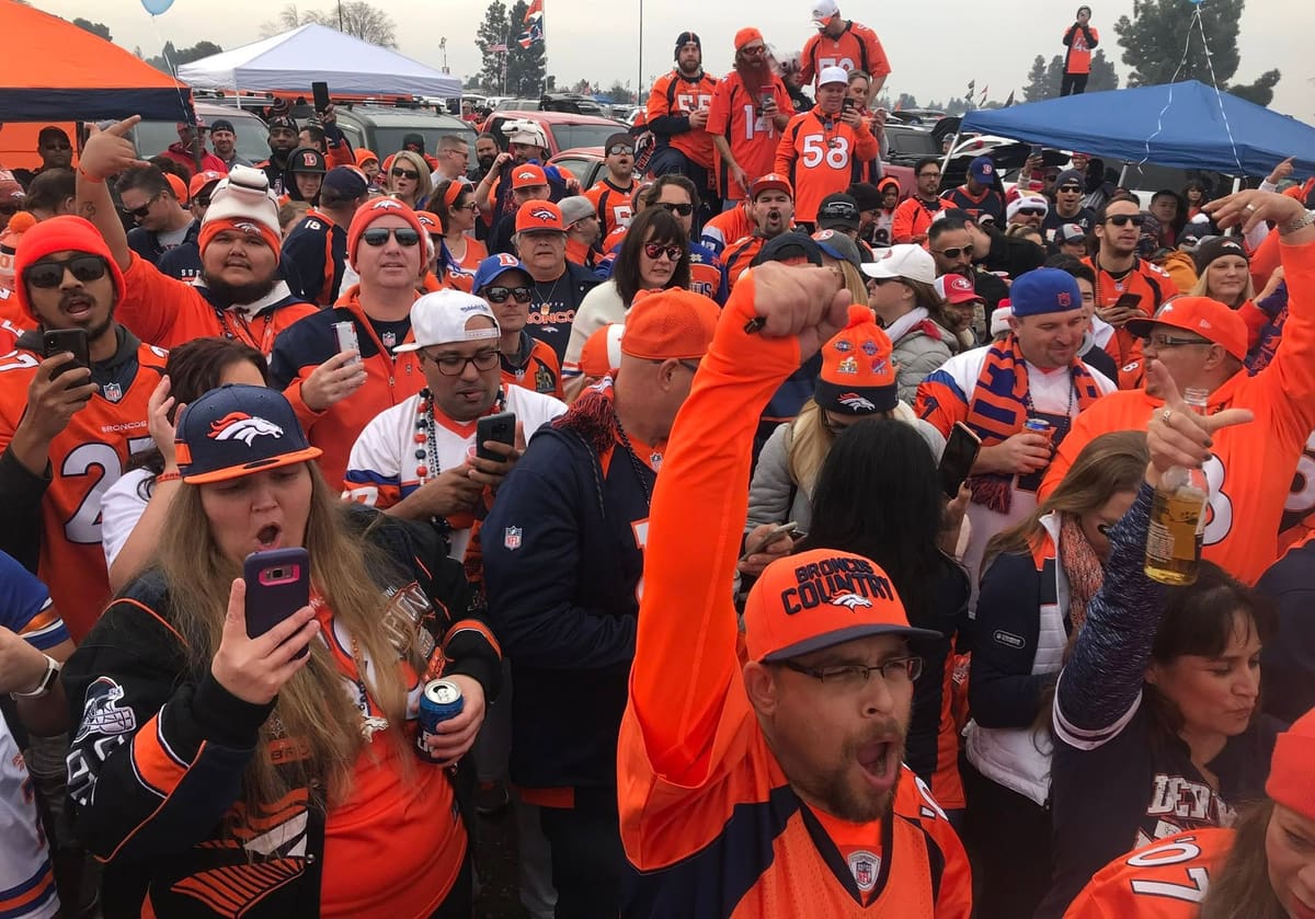 Crowd of Broncos fans in orange cheering in the lot
